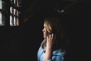 Woman looking out of a dark room through a window. Pondering which opinions are the most valuable opinions.